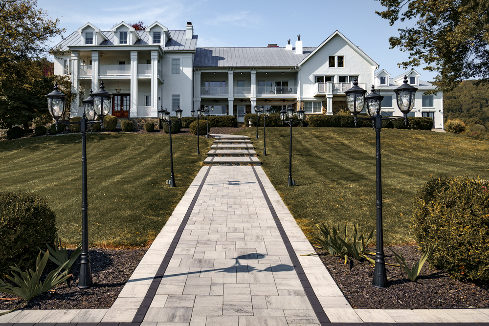 A grand white southern mansion with pillars and a long stone walkway leading to the entrance on a manicured lawn.