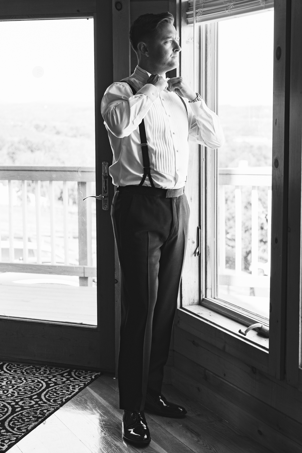 A classic black and white portrait of someone adjusting their bowtie by a window.