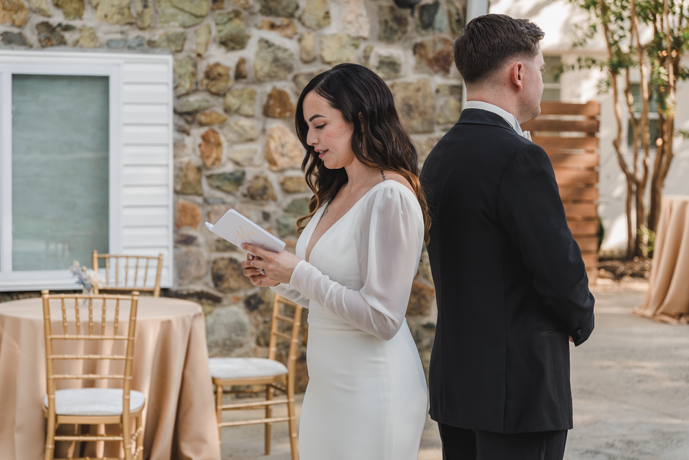 Bride and groom stand back to back looking at their phones during a wedding celebration.