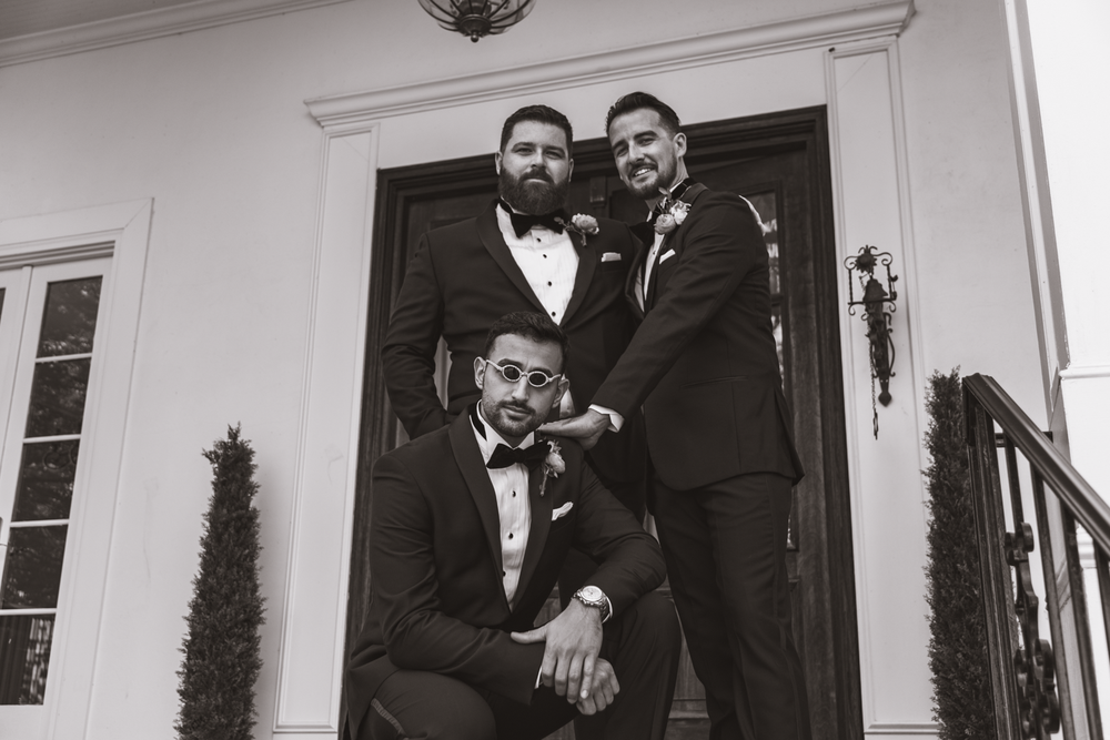 Three groomsmen in black tuxedos pose together in an elegant doorway.