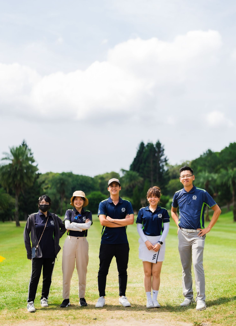 A group of five people in golf attire standing together on a grassy course.