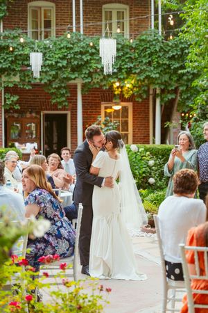A couple shares their first kiss during an outdoor garden wedding ceremony as guests look on.