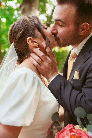 A romantic wedding kiss captured in a garden setting with the bride in a white dress and groom in a dark suit.