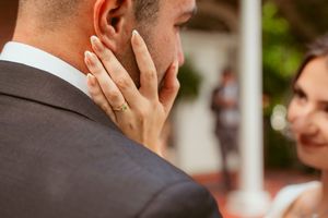 Close up view of hand wearing wedding band caressing cheek against blurred outdoor background.