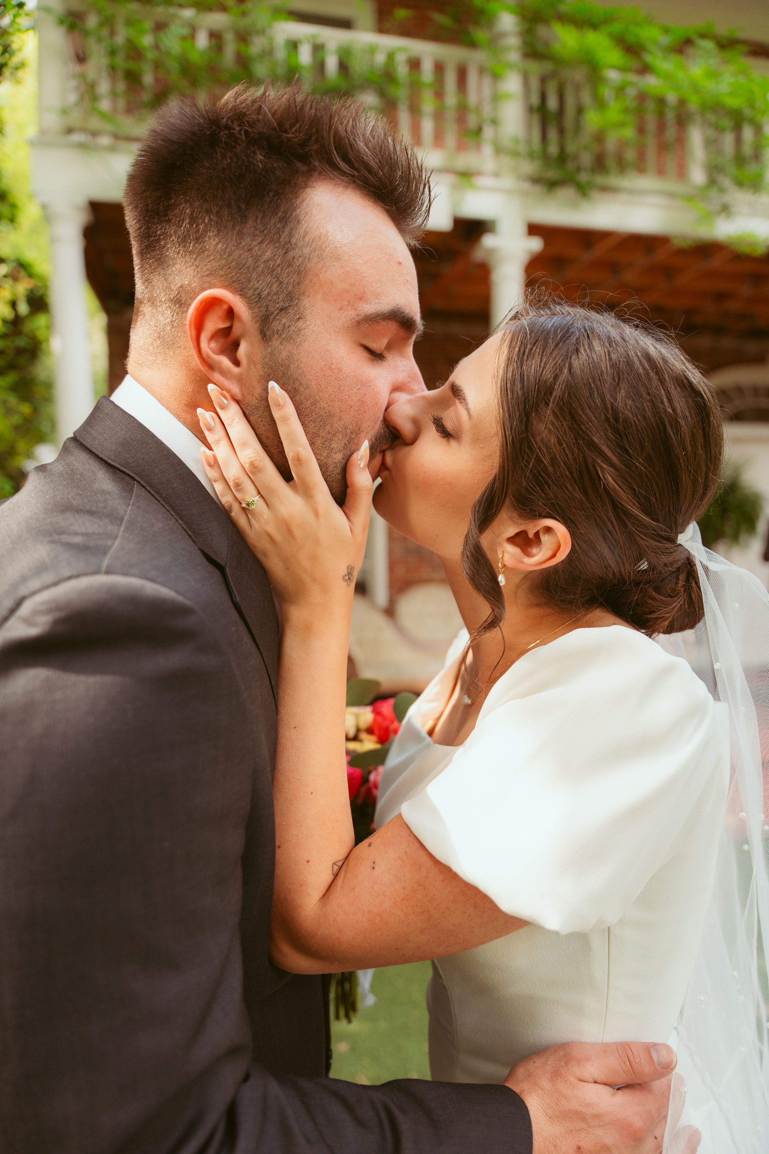A romantic wedding couple sharing their first kiss outdoors with the bride in white and groom in black suit.