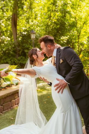 A romantic wedding moment captured in a lush garden setting with natural sunlight filtering through green foliage.