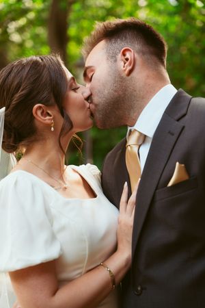 Newlyweds in an intimate close-up kiss moment outdoors with a natural green background.