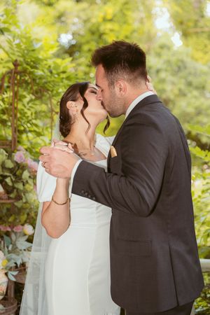 A romantic wedding couple shares a tender kiss in a sunlit garden with lush greenery in the background.