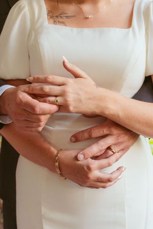 Close-up shot of hands with wedding rings and jewelry against a white dress.