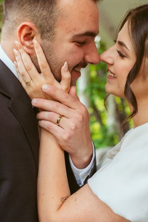 Close-up photo of newlyweds sharing an intimate moment while showing their wedding rings.