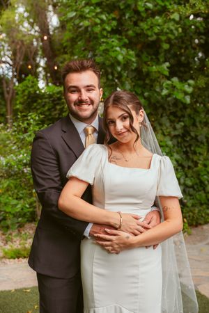 Wedding couple in formal attire posing together against a leafy green background.