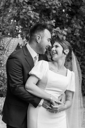Black and white portrait of a joyful wedding couple embracing and laughing together outdoors.