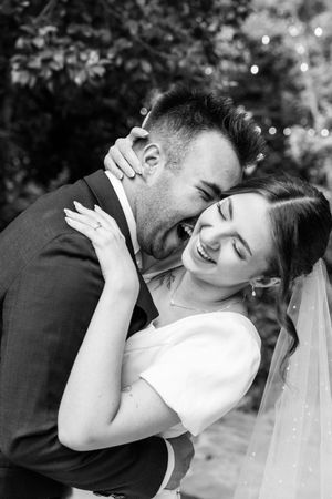A black and white wedding photo captures a joyful moment between newlyweds as they laugh together.
