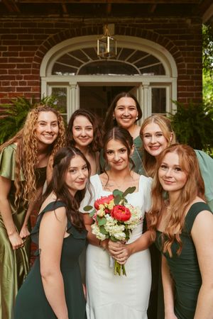 A joyful wedding party poses in front of a classic red brick building with white trim.