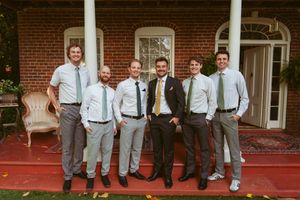 Group of groomsmen in grey slacks and white shirts posing on brick porch with red flooring.
