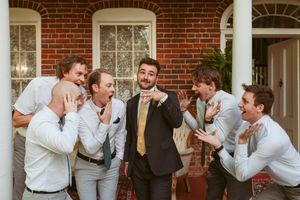 Joyful wedding party laughing together on brick porch during candid moment.
