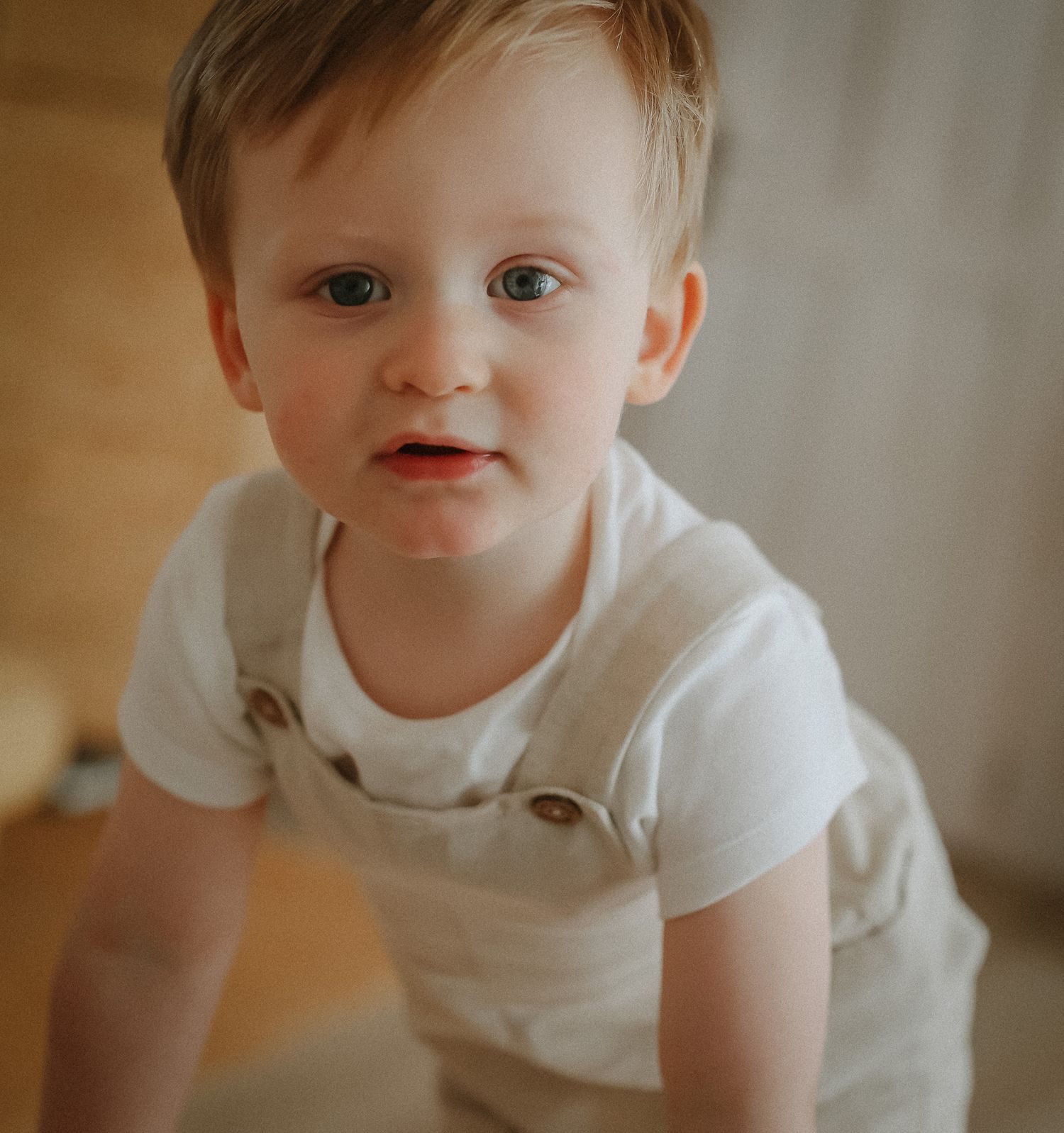 Small child in white shirt crawls and explores on hardwood floor in warm indoor lighting.