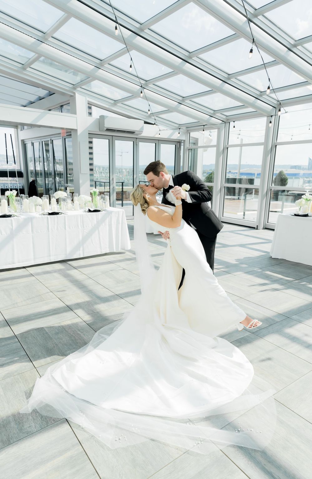 A romantic dip pose in a modern glass-ceiling venue with city views.