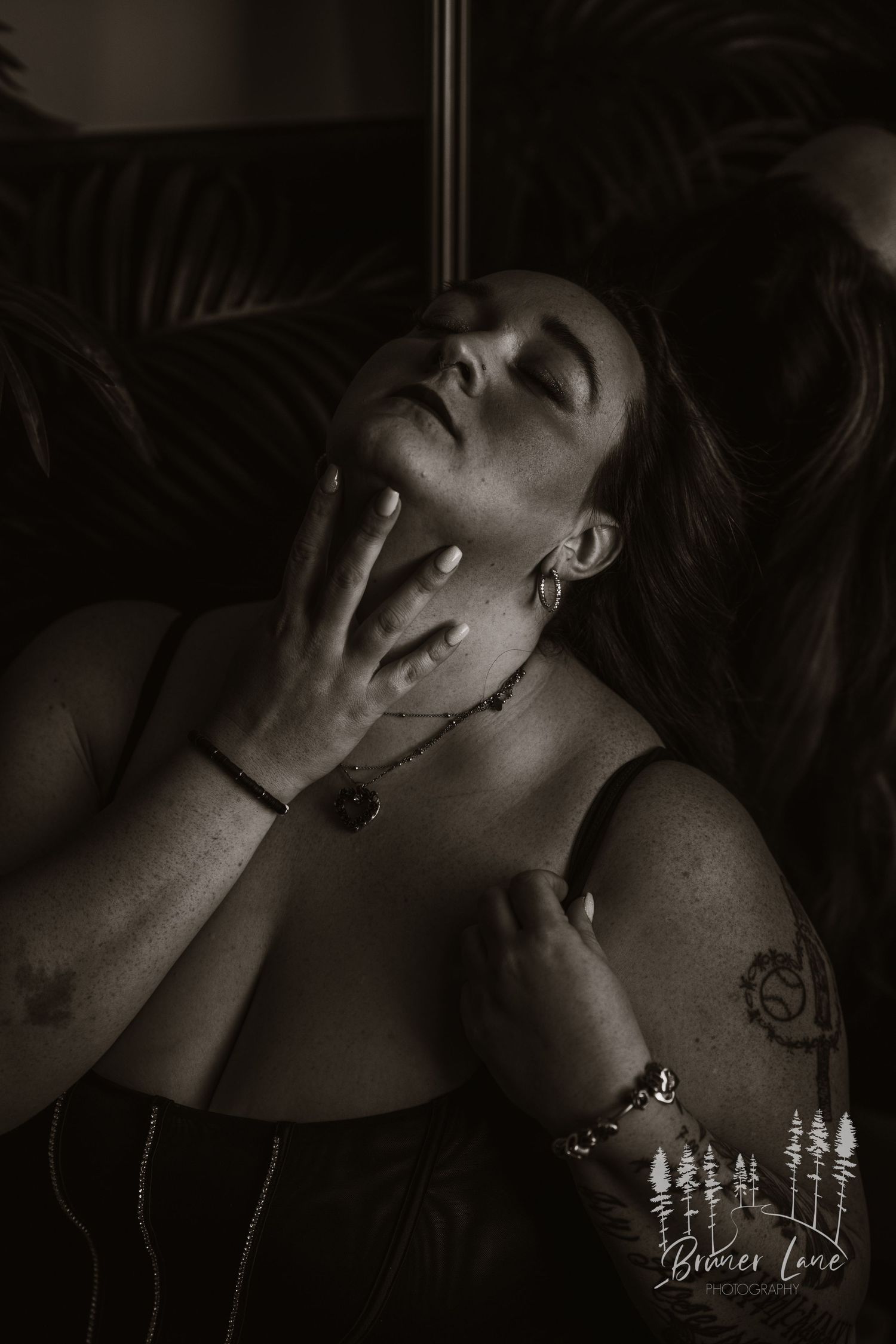 A monochromatic portrait shows figure with closed eyes and raised hand against palm leaves in dark, moody lighting.