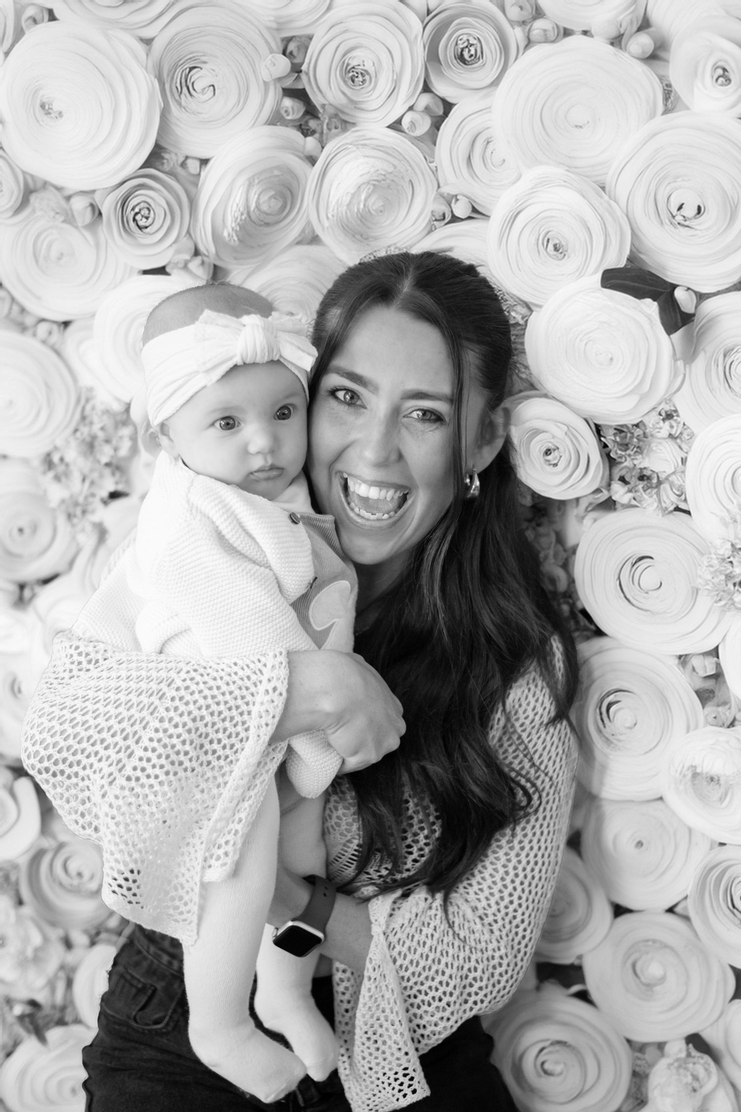 Black and white portrait in front of a floral backdrop of white paper roses.
