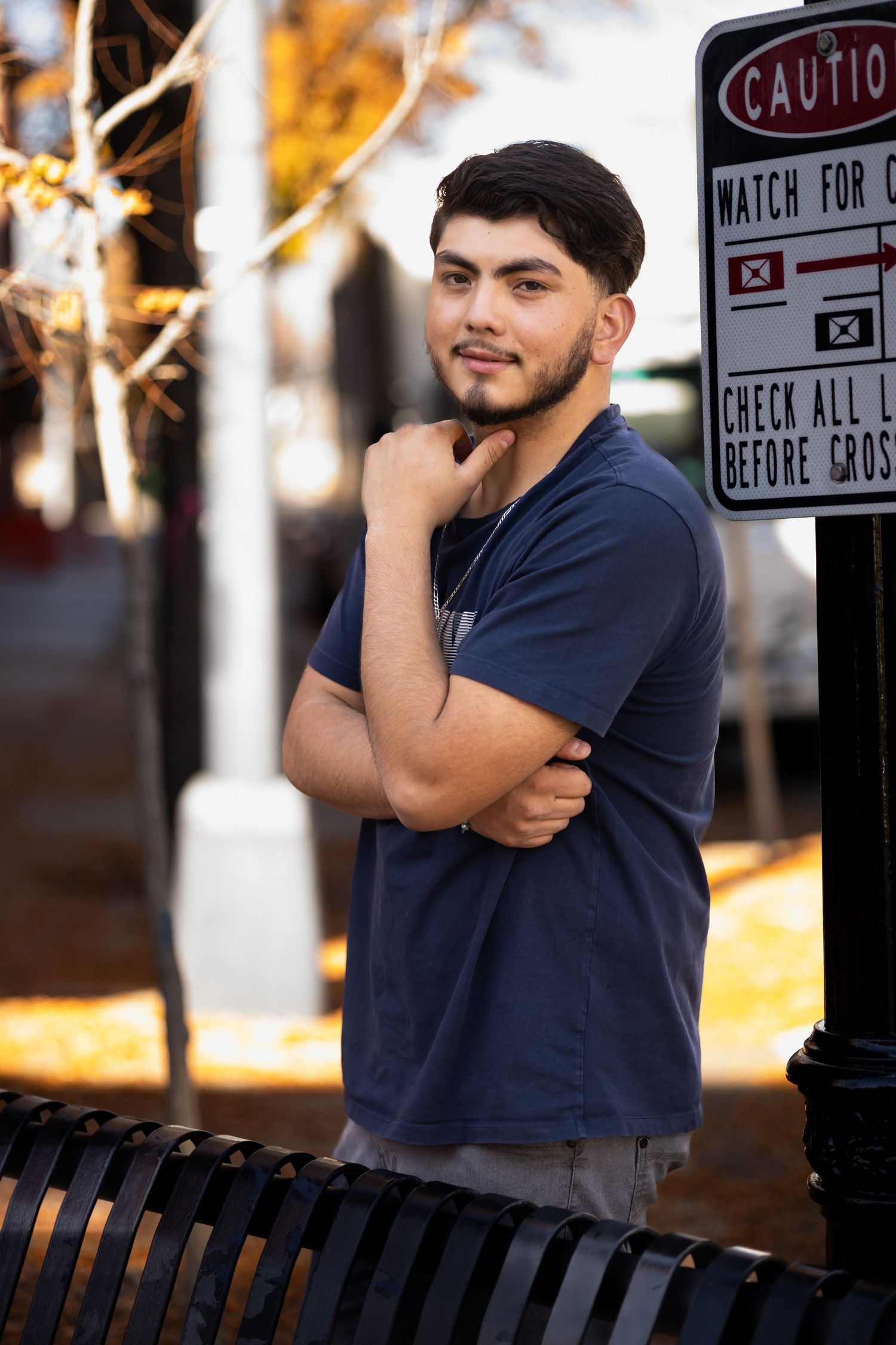 A person in a navy blue t-shirt poses thoughtfully near a caution sign on a sunny autumn day.