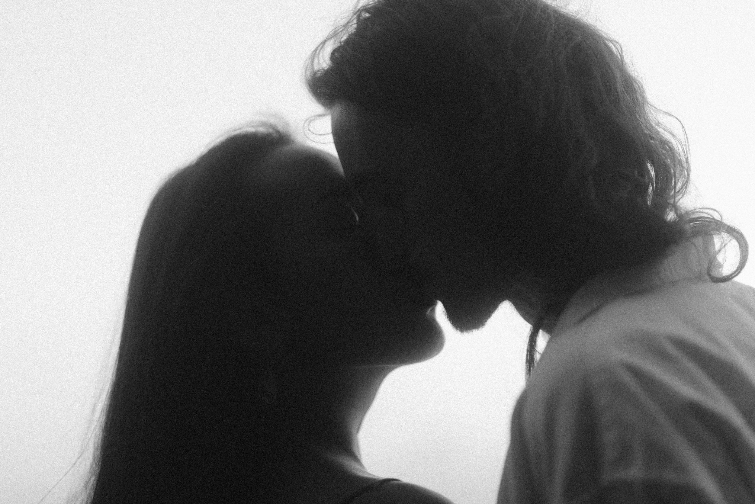 An intimate black and white silhouette portrait of a couple in a tender moment with soft lighting and gentle shadows.
