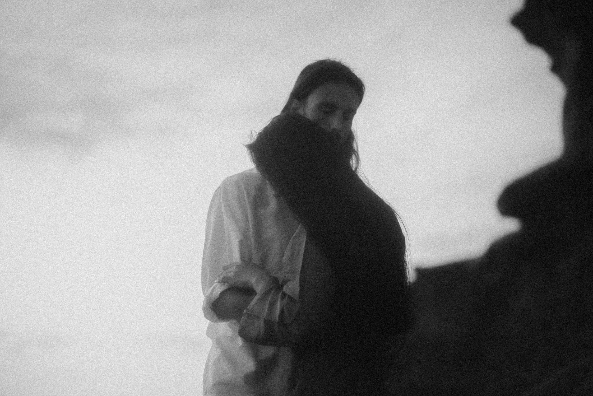 Atmospheric black and white silhouette of two figures standing together in moody lighting.