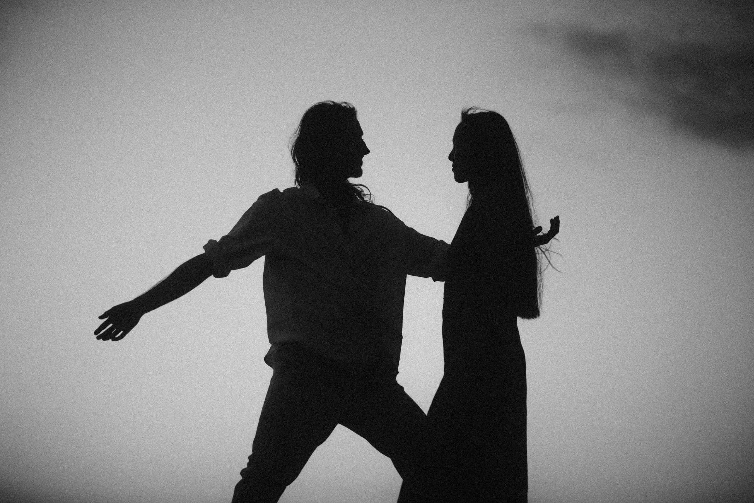 Dramatic silhouette of two dancers in motion against a misty light background.
