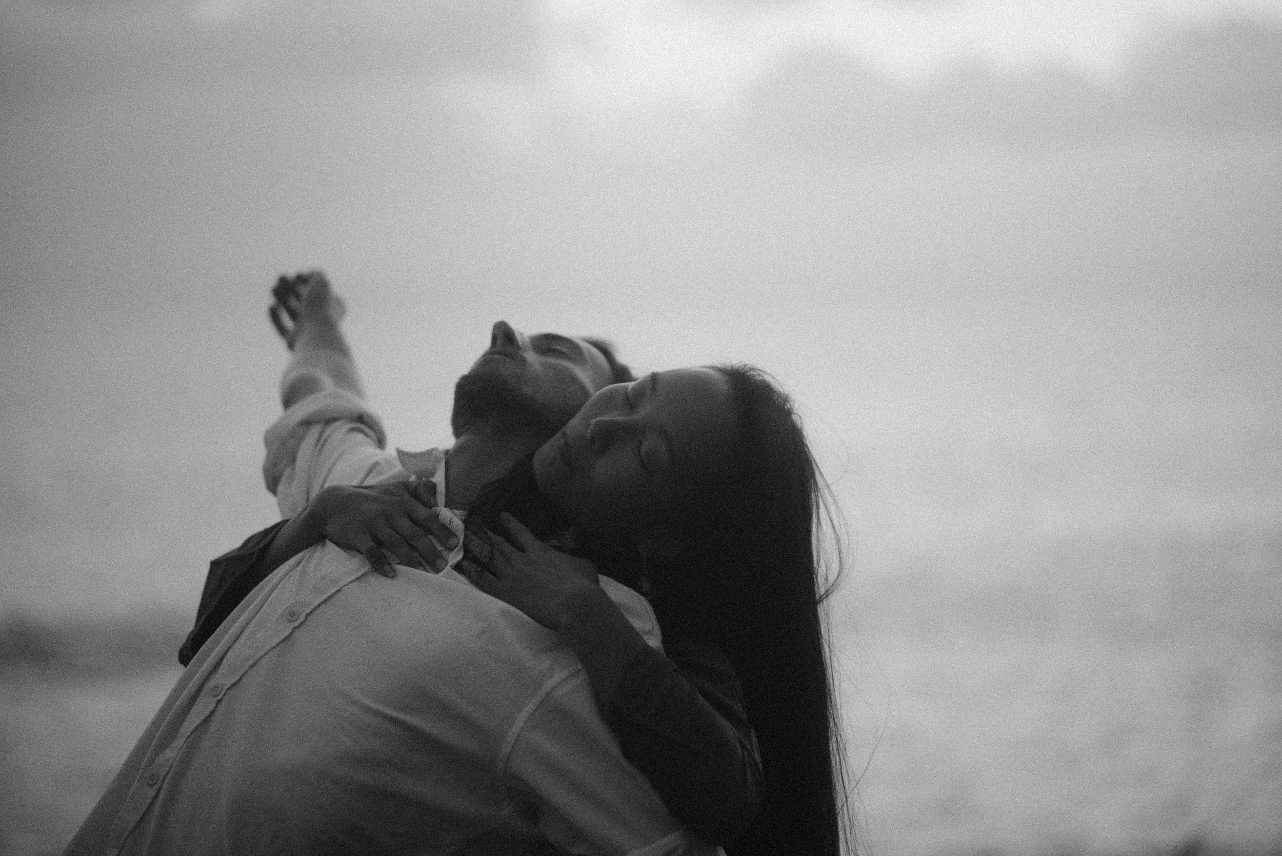 A grayscale photo of a person leaning back under a cloudy sky.