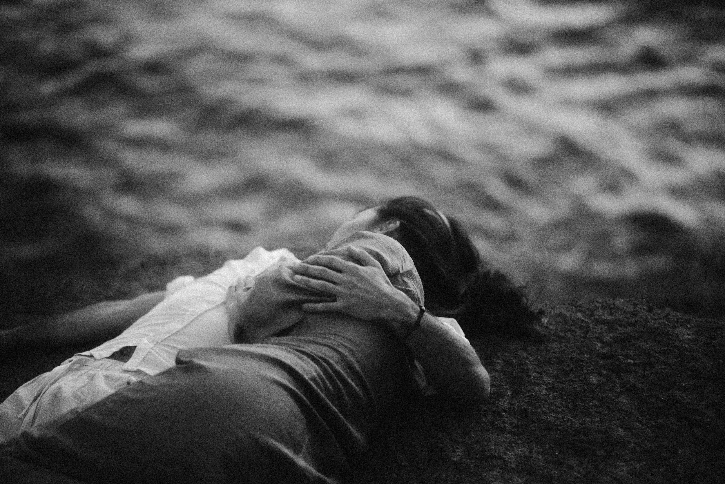 Black and white photograph of someone reclining by water with dramatic lighting and reflective surface.