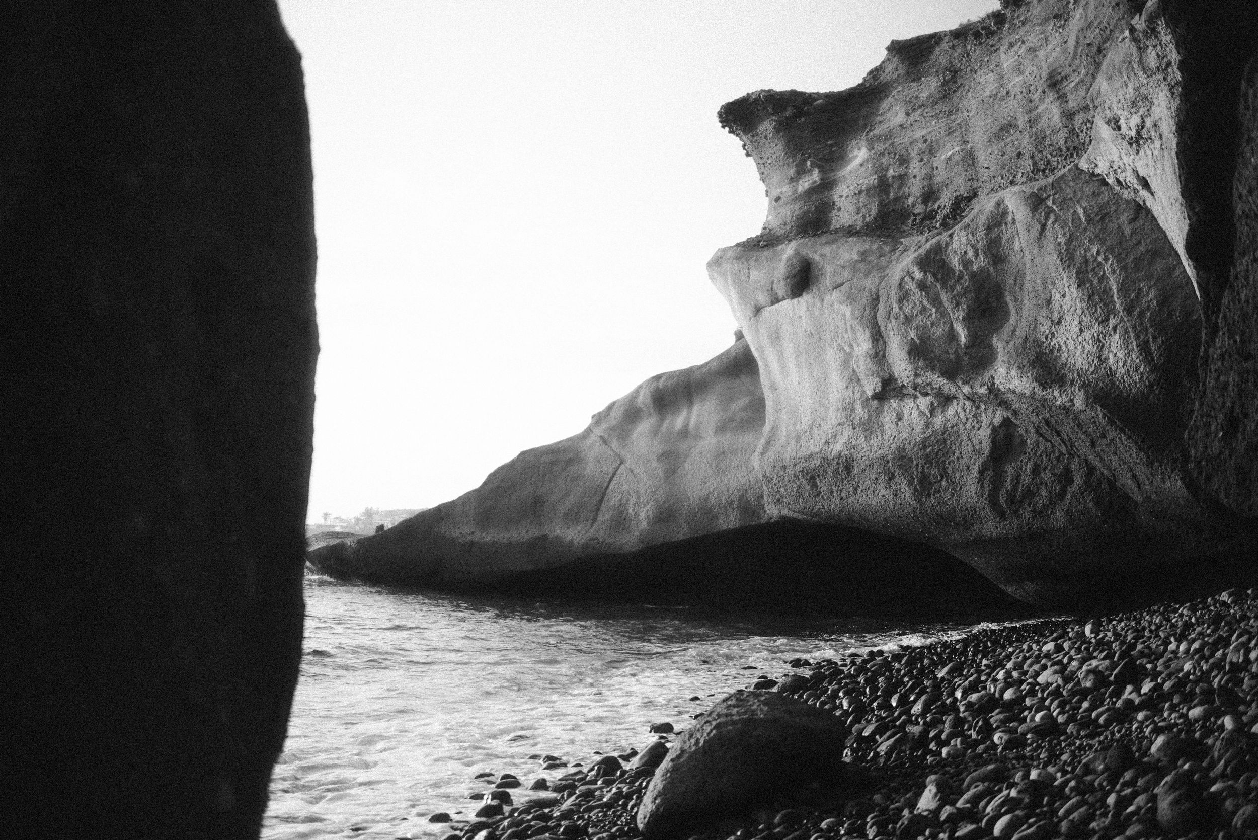 Dramatic black and white coastal landscape with steep white cliffs and rocky beach along the water's edge.