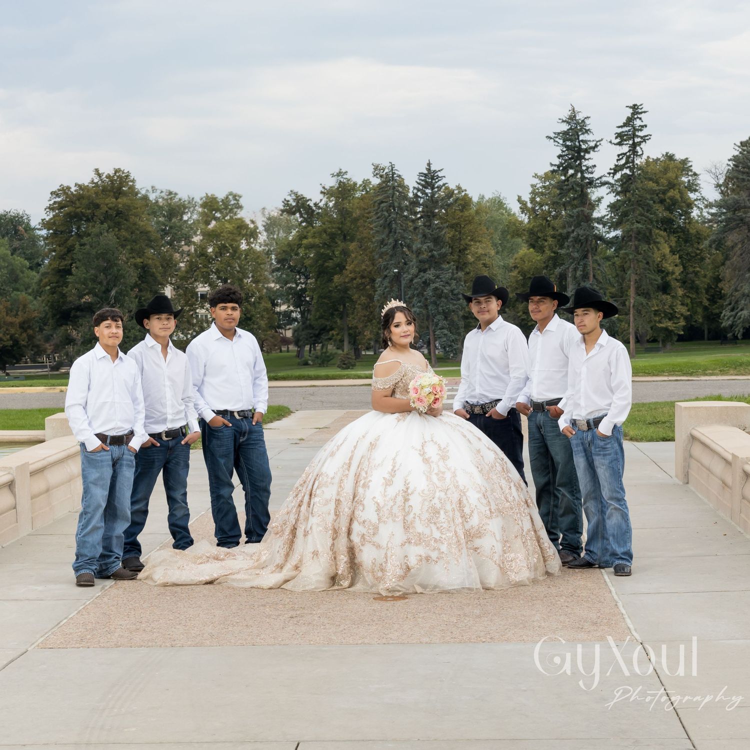 A quinceañera celebration scene with people in western attire and a person in an elegant champagne-colored ballgown on steps.