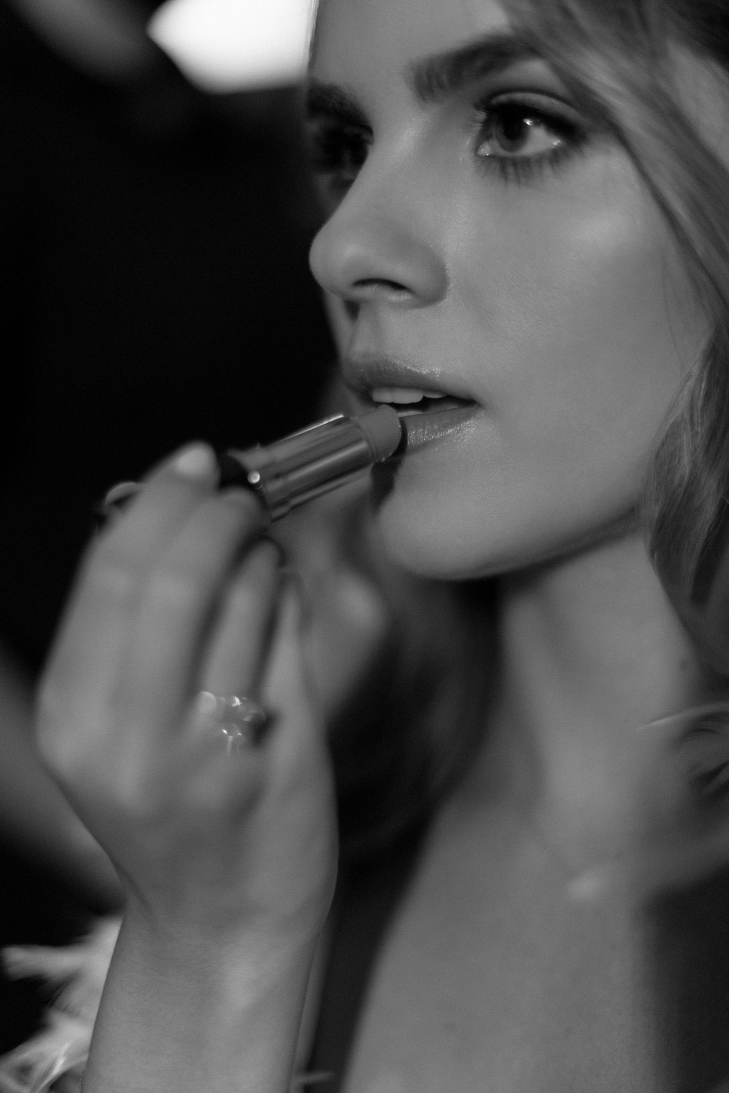 Black and white photo of someone applying lipstick in a soft, elegant makeup moment.