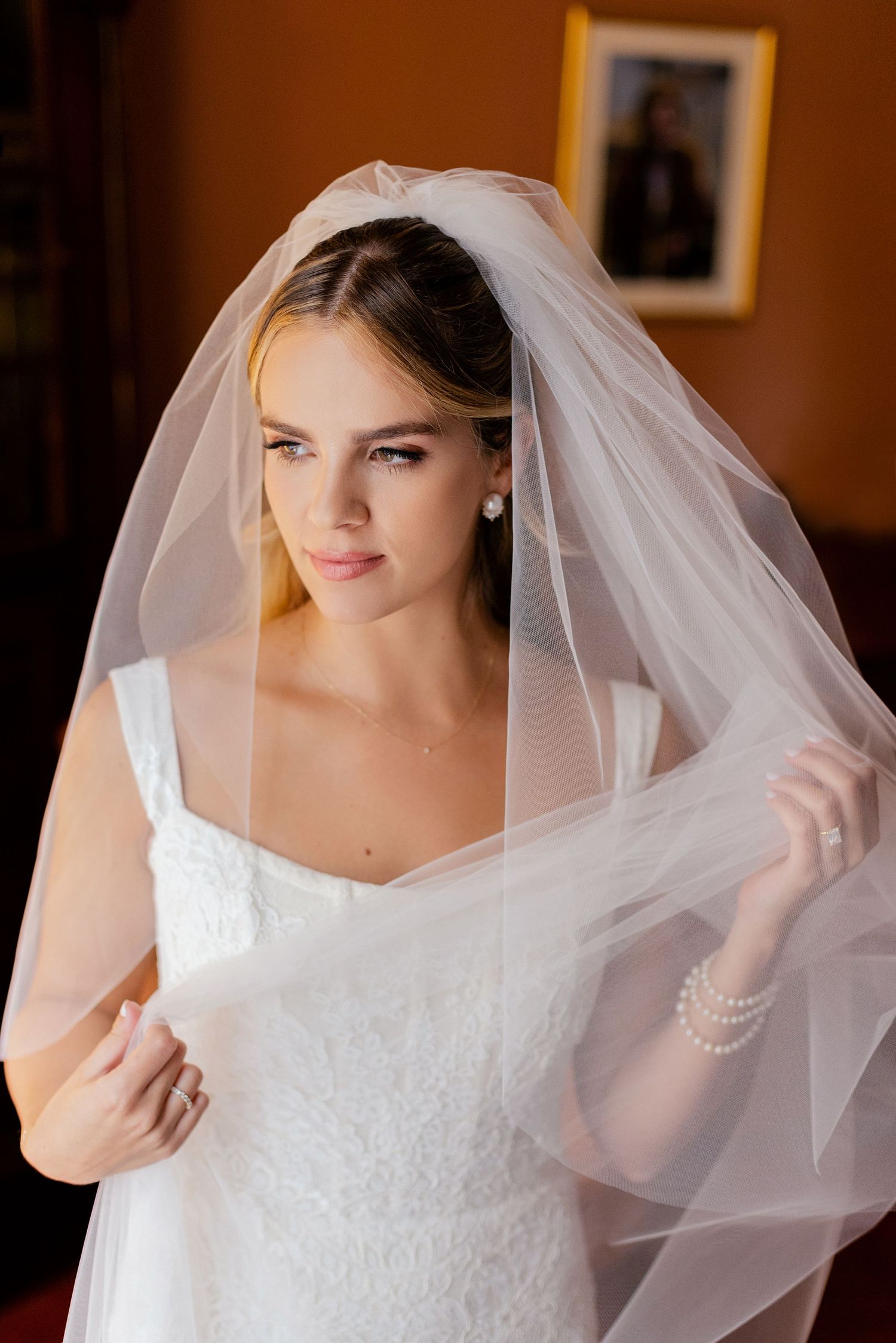 Bride wearing a traditional white lace dress and veil in a warmly lit room.