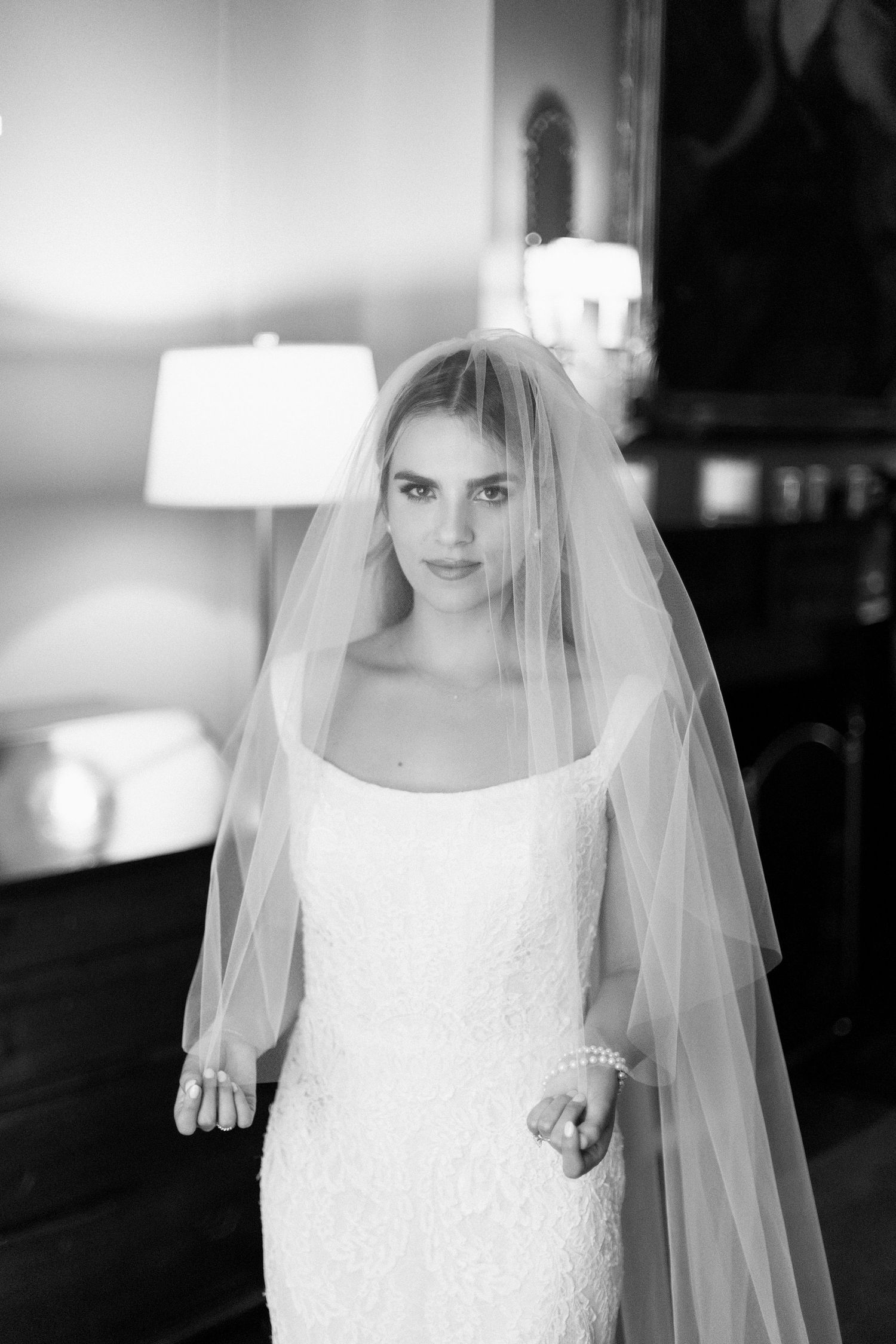 A bride poses in an elegant white wedding dress with a flowing veil in a classic black and white portrait.