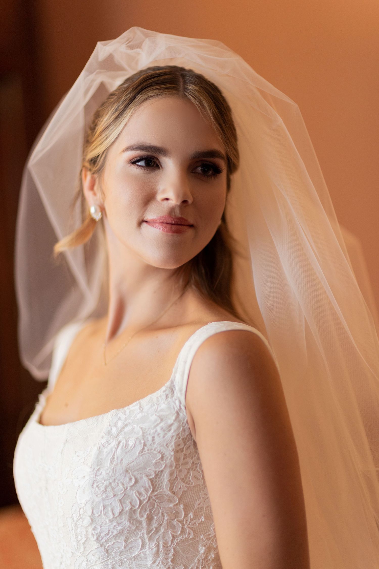 A bride wearing a lace gown and long veil poses in beautiful natural lighting.
