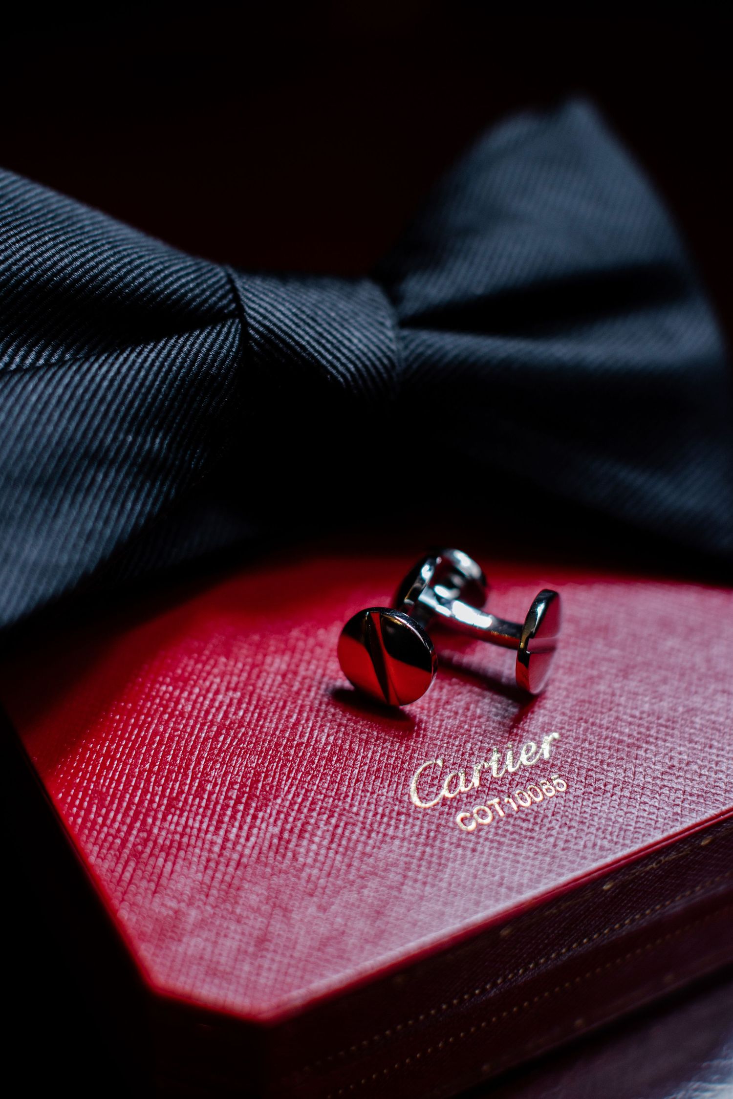 Elegant black bow tie and silver cufflinks resting on a red Cartier jewelry box.
