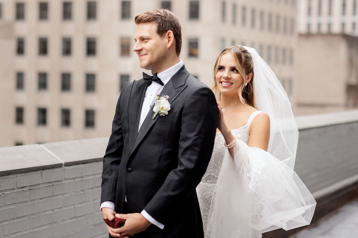 Newlyweds stand together on rooftop with city buildings in background.