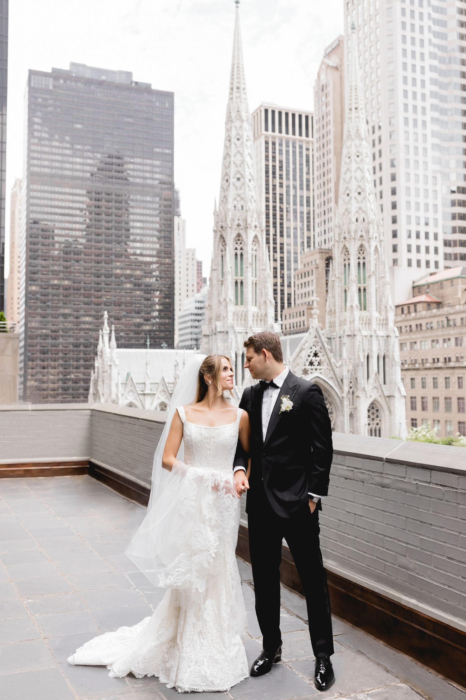 Newlyweds pose for a portrait on a rooftop with St. Patrick's Cathedral and Manhattan skyline in the background.