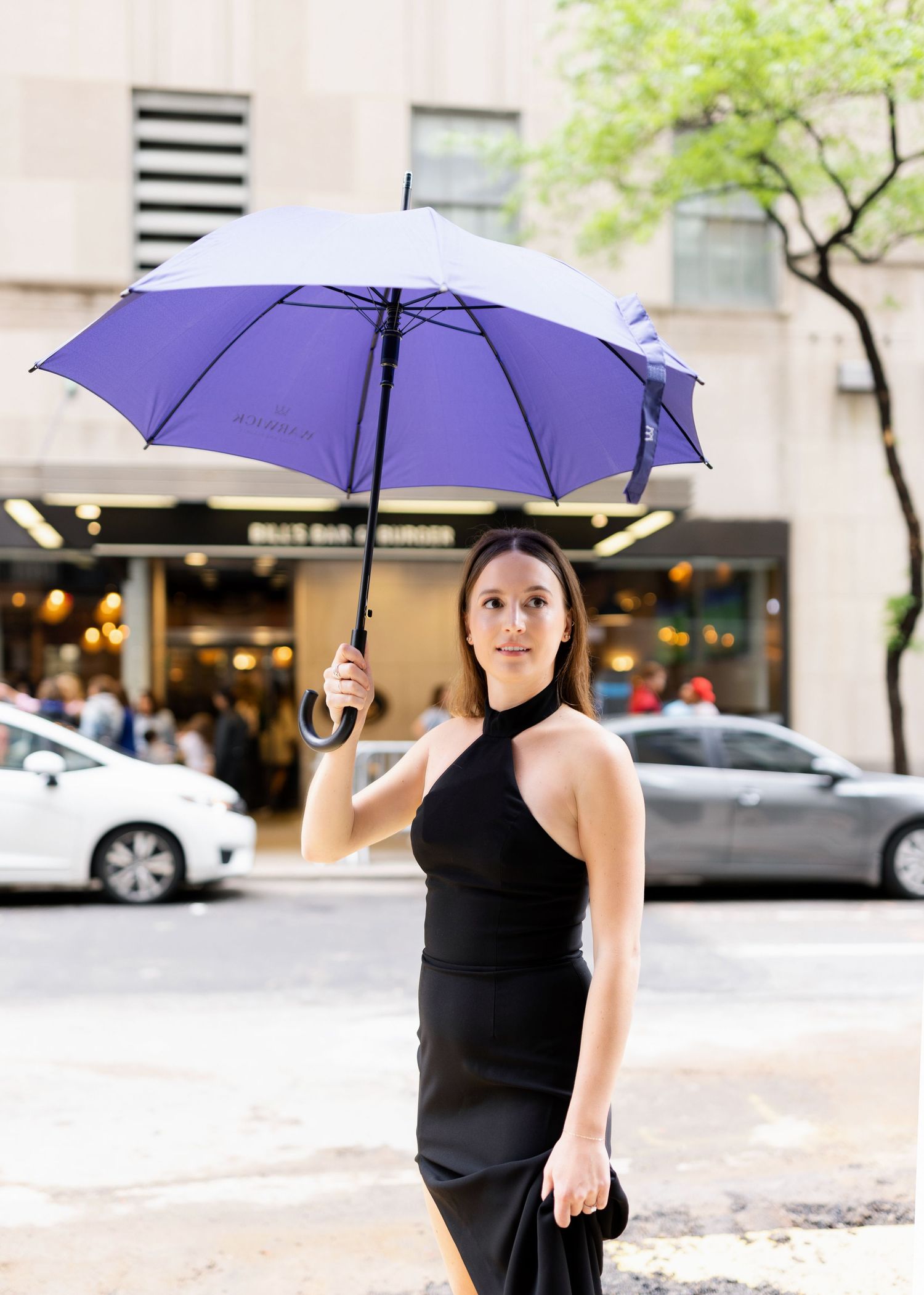Woman in black dress holding purple umbrella on city street.