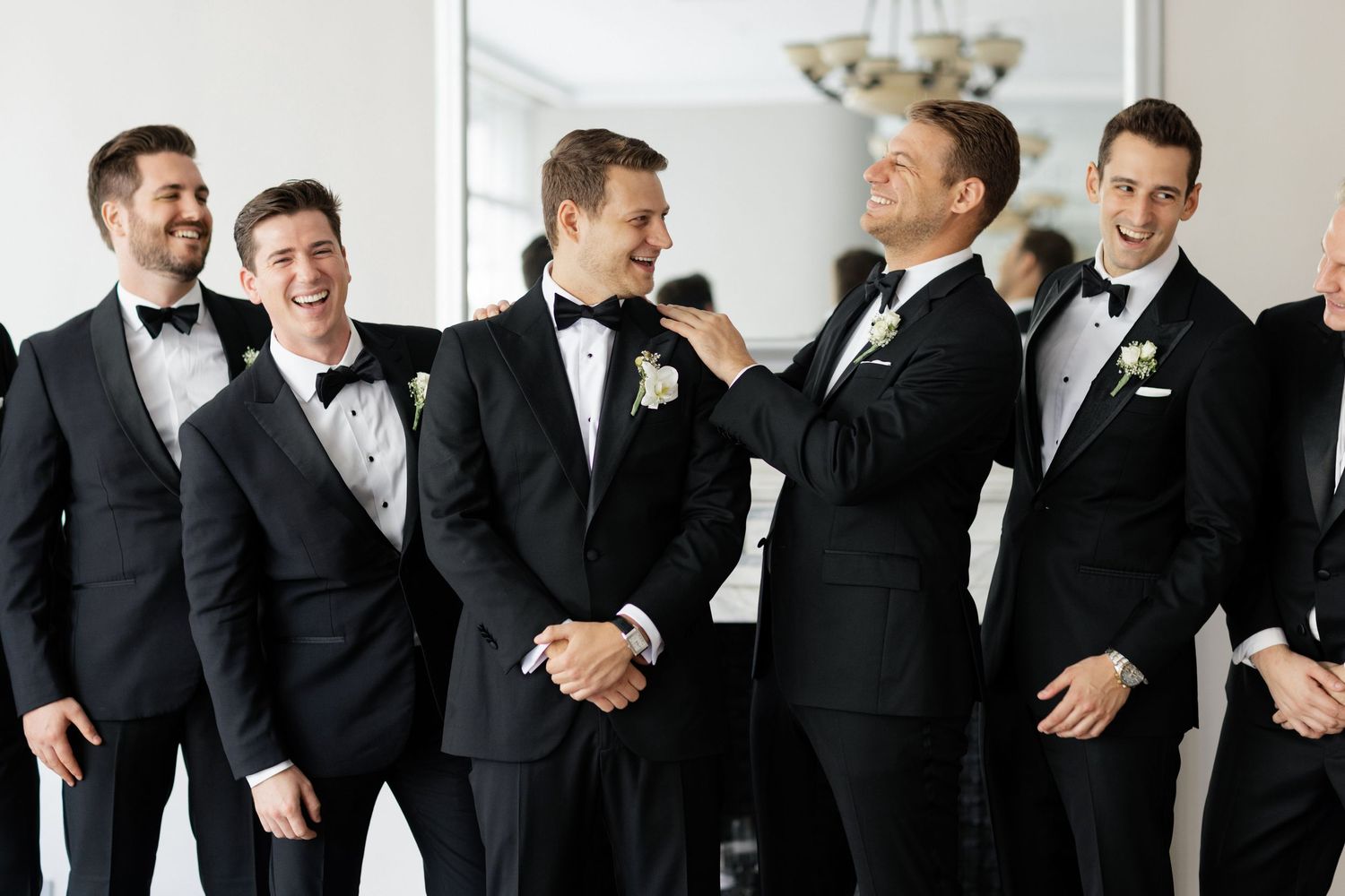 Groomsmen in black tuxedos share a lighthearted moment before the wedding ceremony.