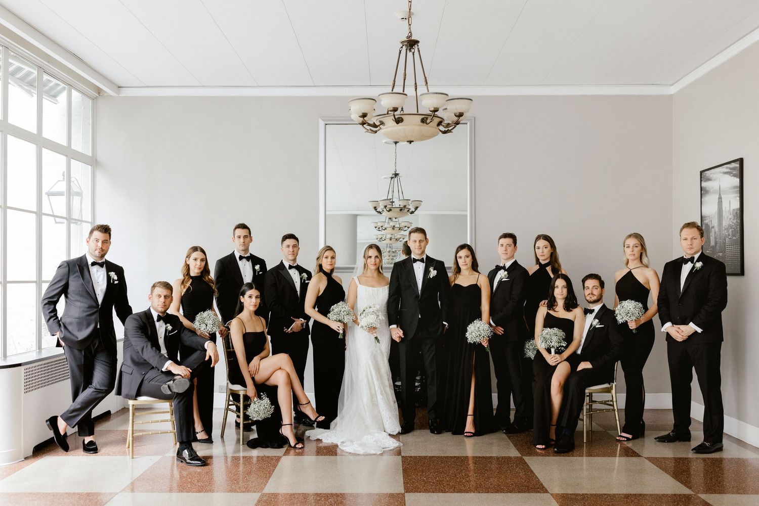 Elegant wedding party in black and white formal attire posed together in bright room with chandelier.