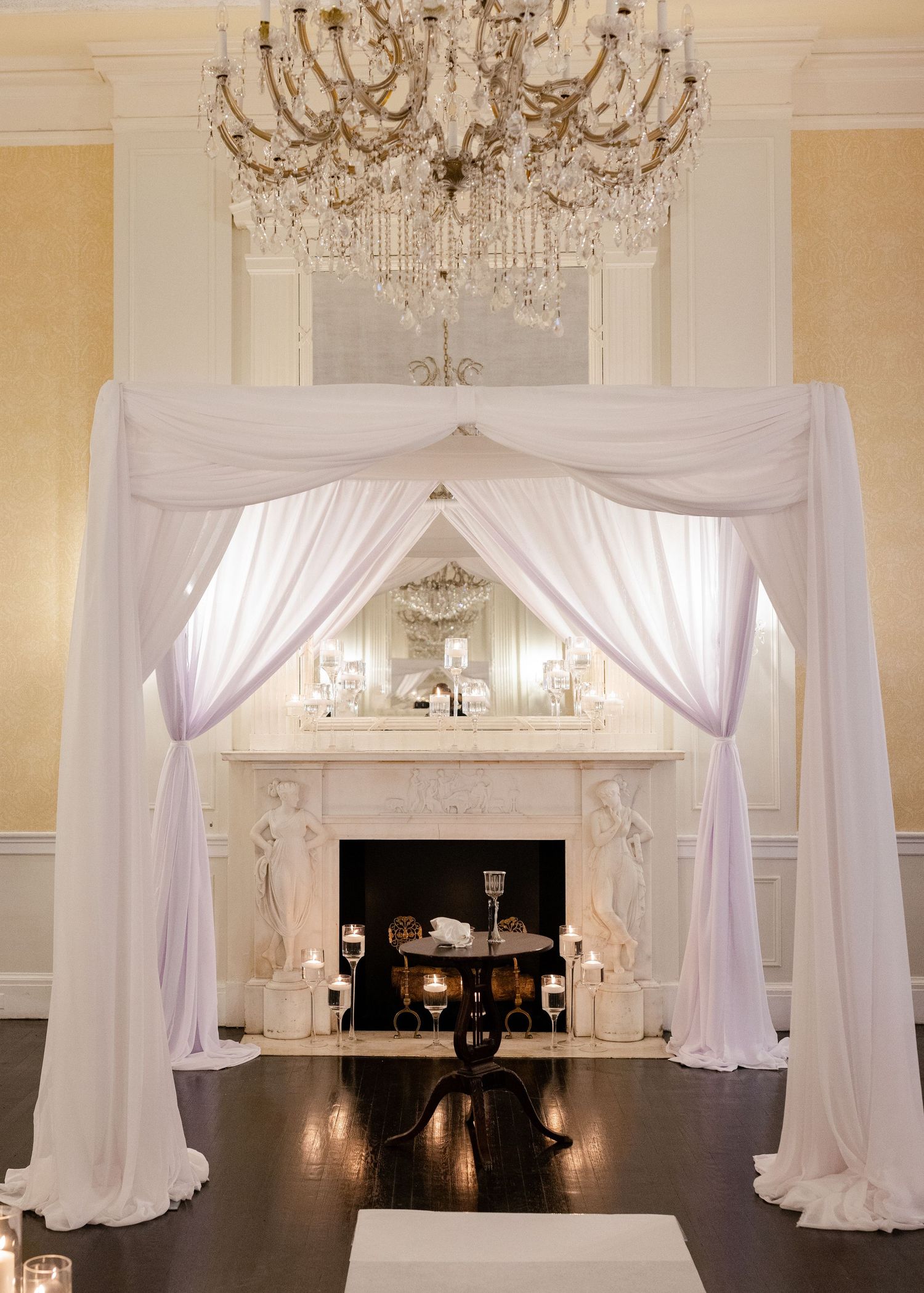 Elegant white fabric draped archway with chandelier and fireplace for wedding ceremony.