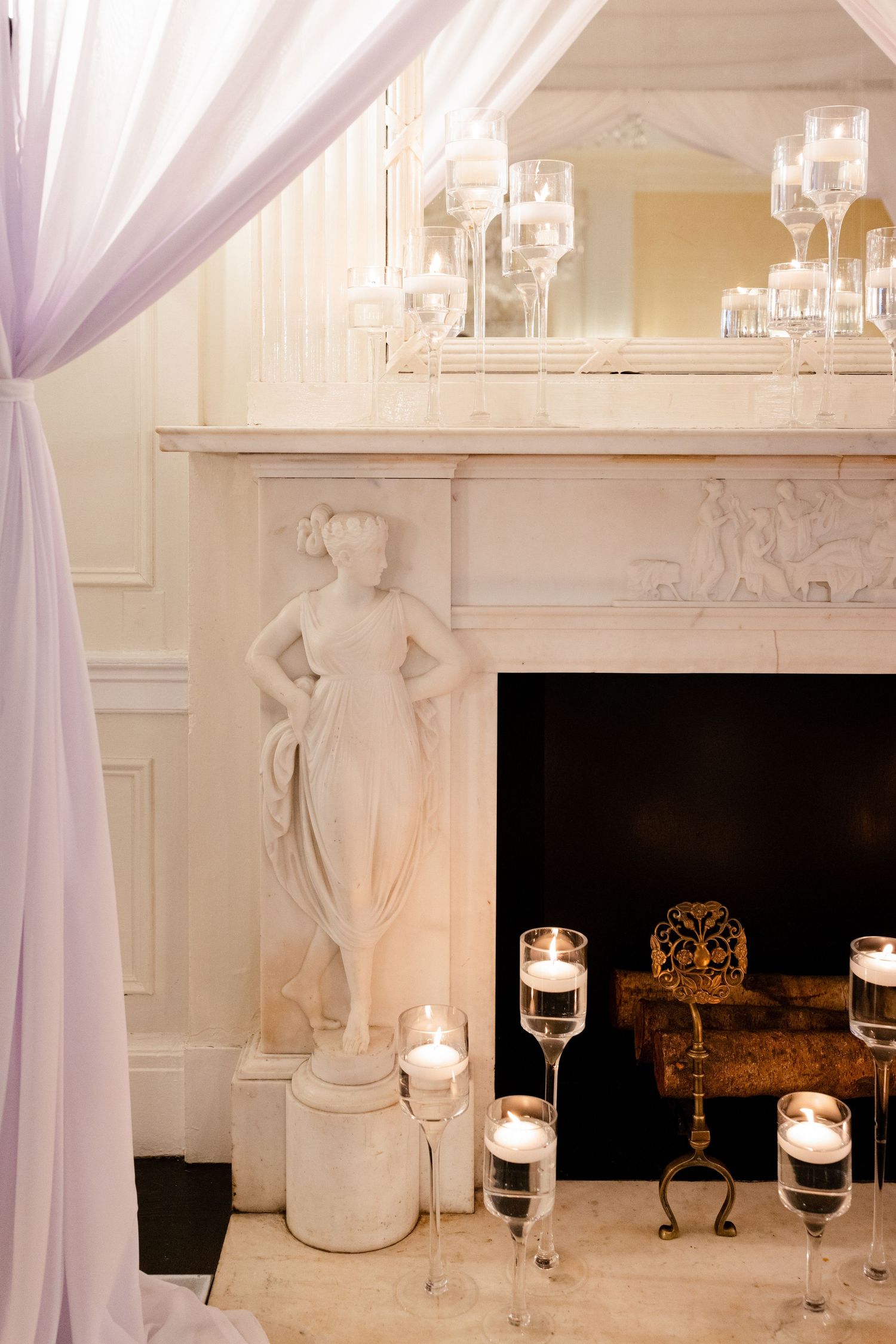 Elegant fireplace mantel decorated with candles and draped fabric for wedding reception.