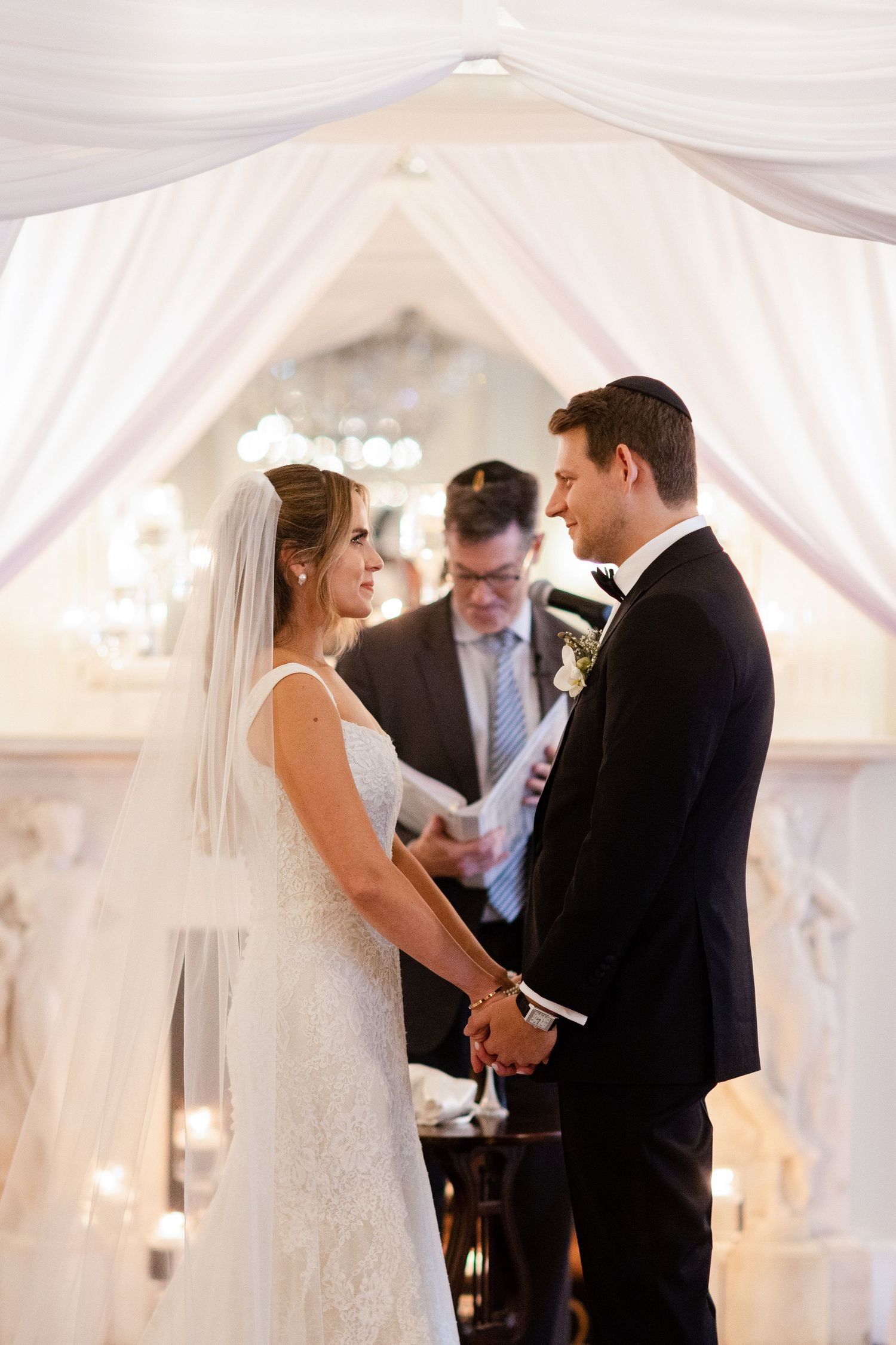 Wedding ceremony under white fabric draping with crystal chandelier.