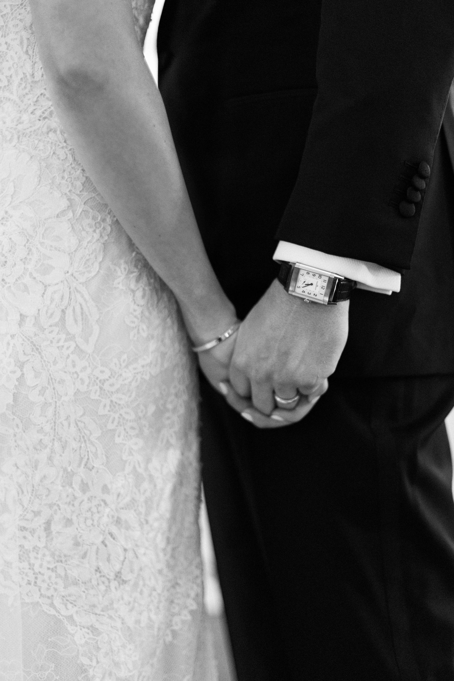 Black and white close-up of couple holding hands showing wedding rings and formal attire.