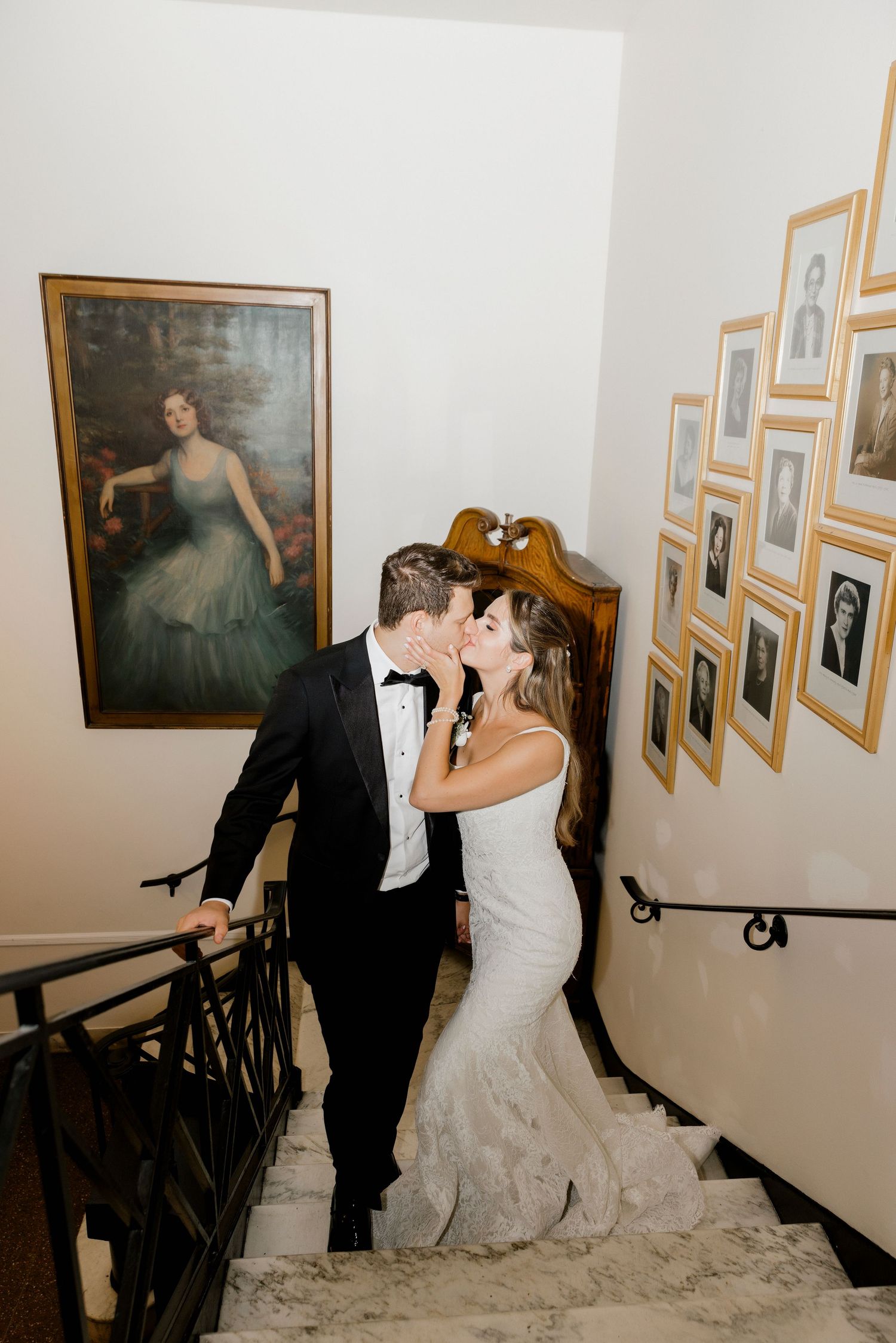 Intimate wedding moment captured on staircase with vintage portrait and gallery wall in background.