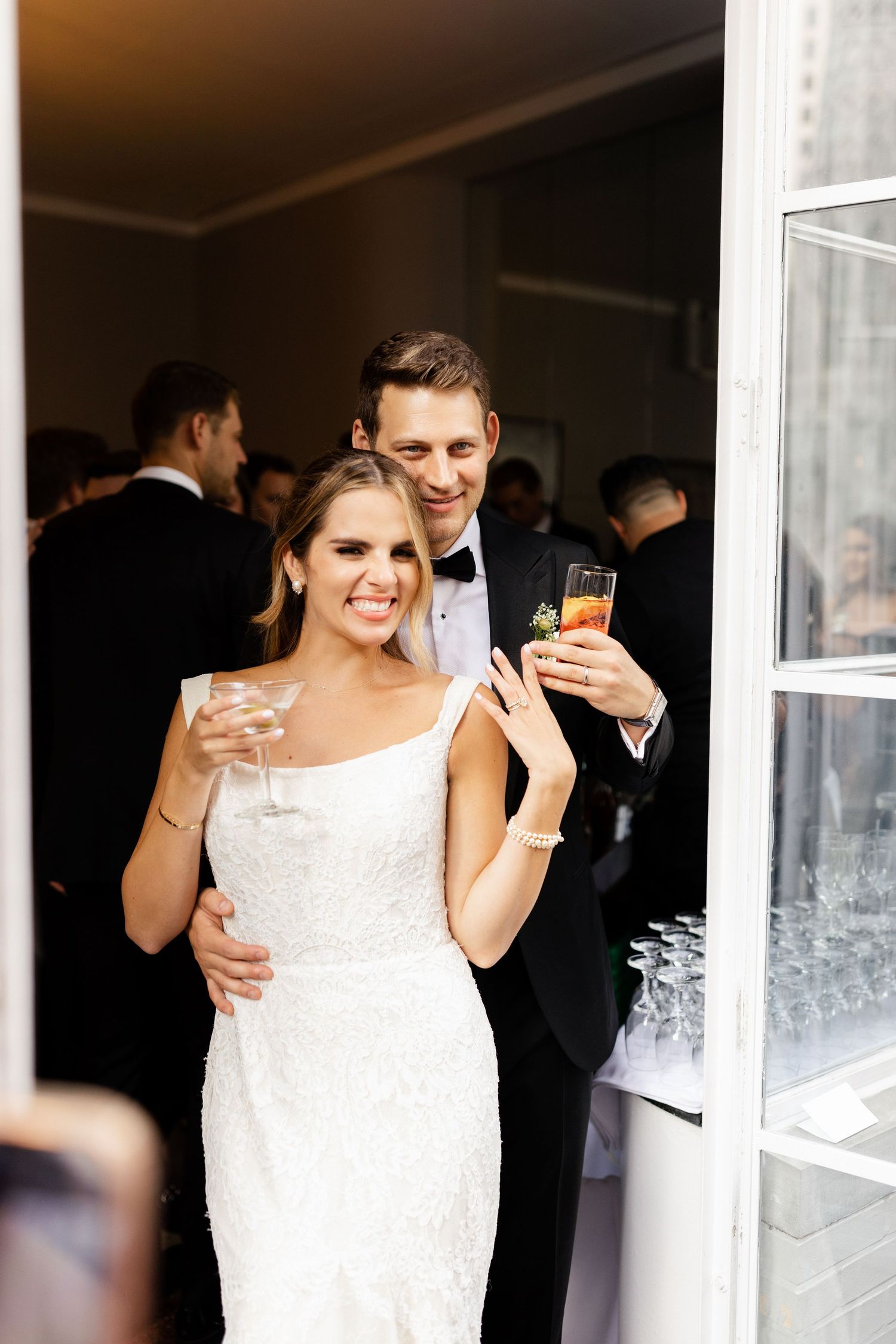 A couple in wedding attire share drinks and smiles during their reception celebration.