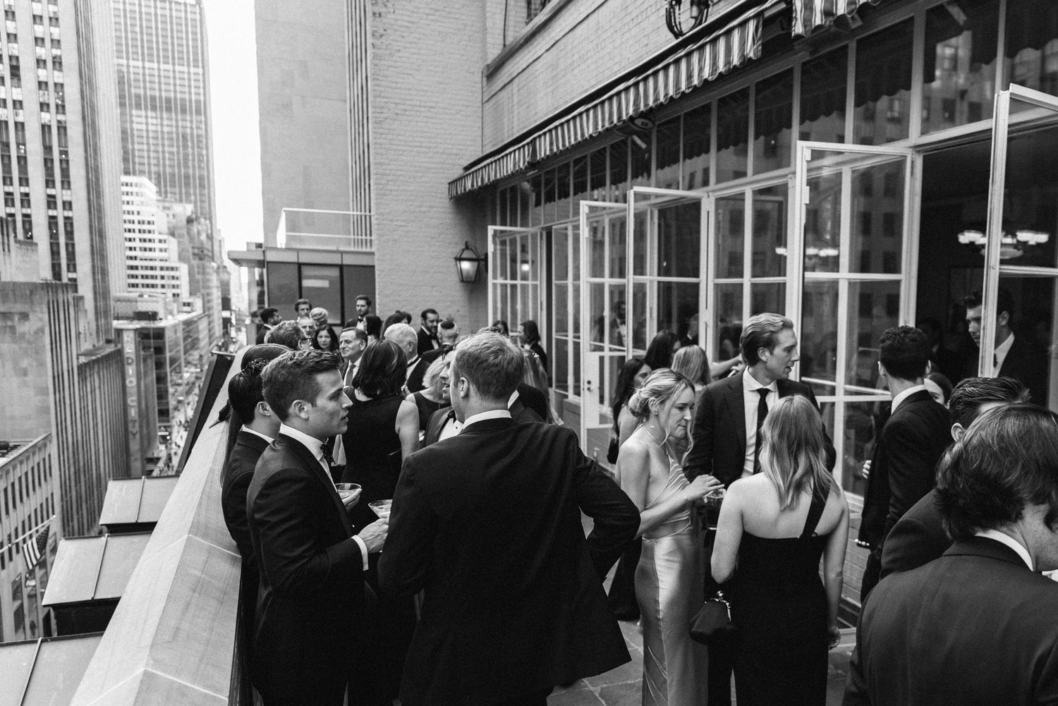 Wedding guests mingle on an urban rooftop terrace in black and white photography.
