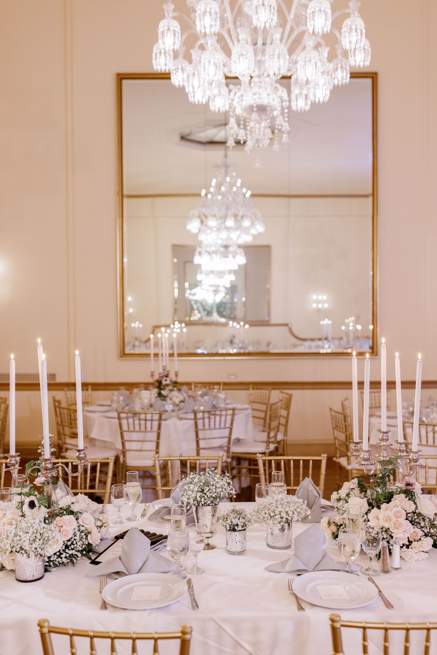 Elegant wedding reception table setting with crystal chandelier and white floral centerpieces.